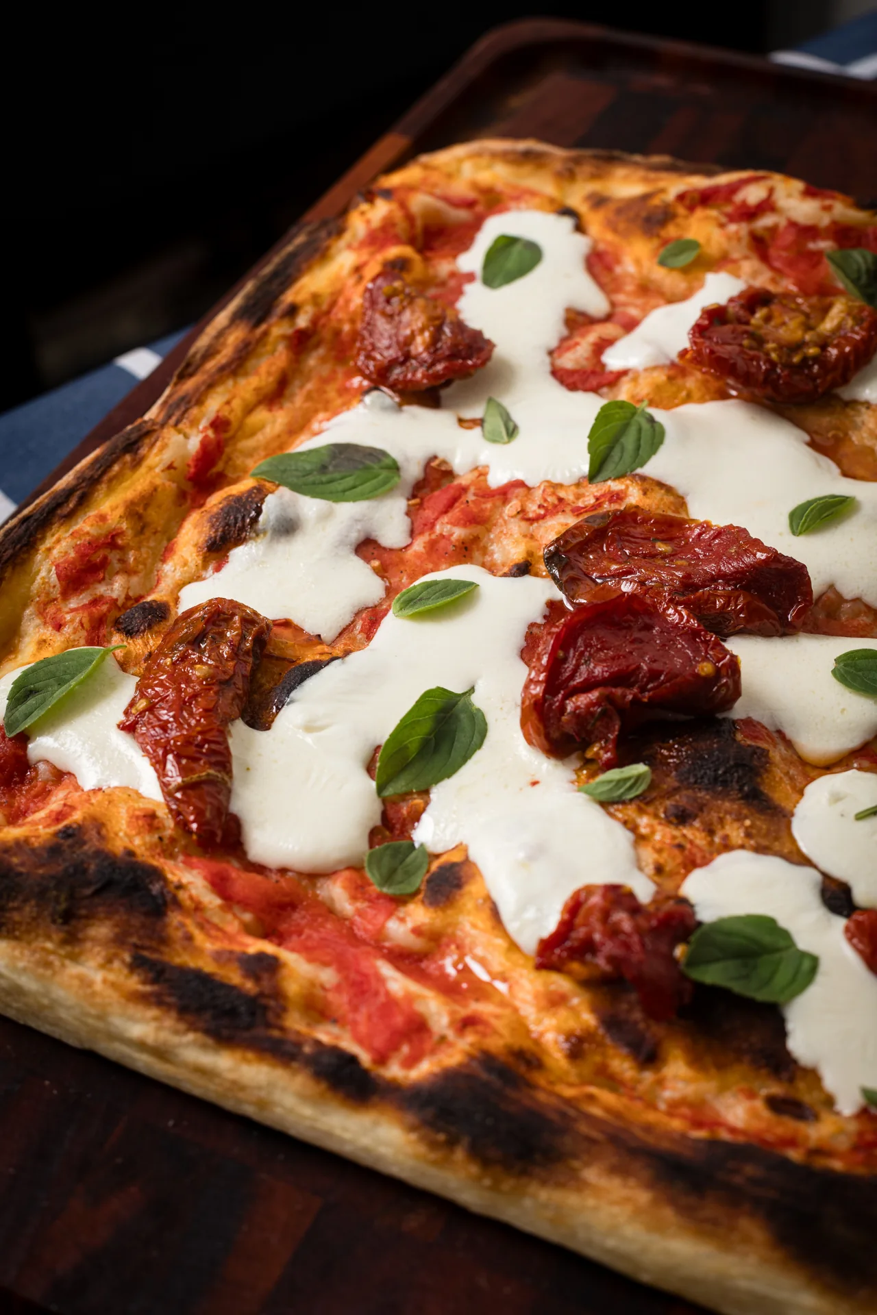 Detalhe da pizza Oficina Lievito: borda dourada, molho de tomate, queijo e folhas de manjericão